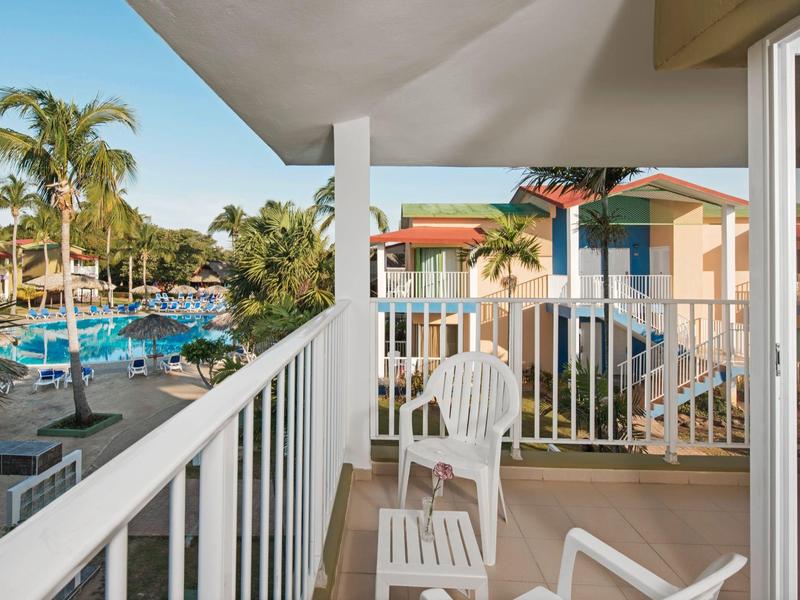 Balcone con sedie che si affaccia su un'area piscina con palme in un resort.
