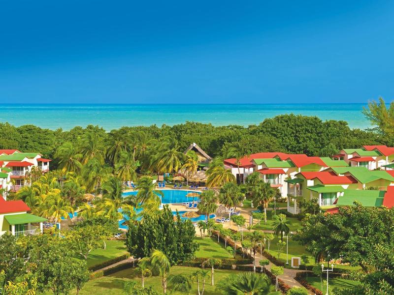 Resort con tetti rossi, palme e piscina vicino al mare sotto un cielo azzurro.