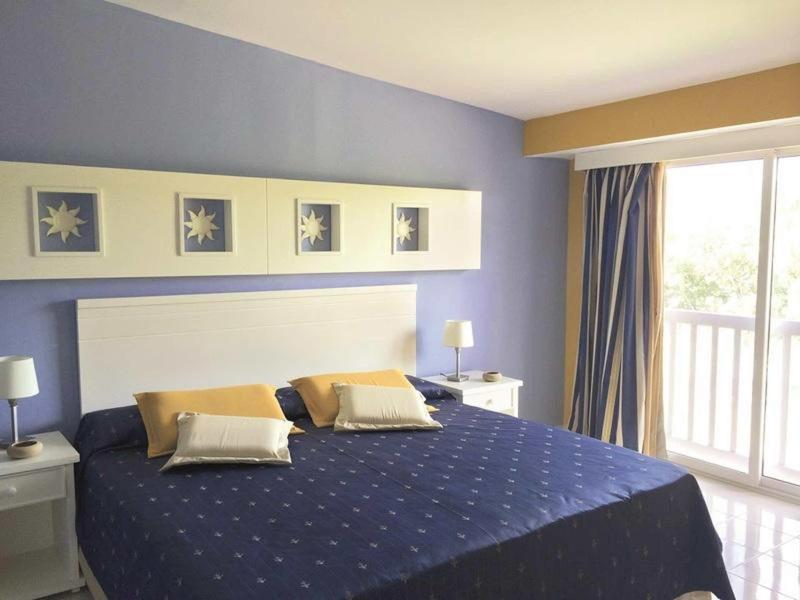 Camera d'hotel luminosa con un grande letto, parete viola e balcone con tende.