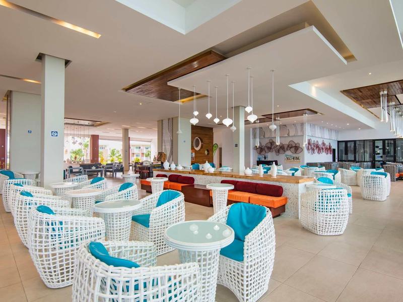 Ampia zona lounge dell'hotel con sedie in vimini bianche e cuscini colorati.