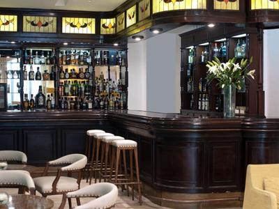 Elegancki bar hotelowy z ciemnego drewna, stołkami barowymi i ozdobnymi kwiatami.