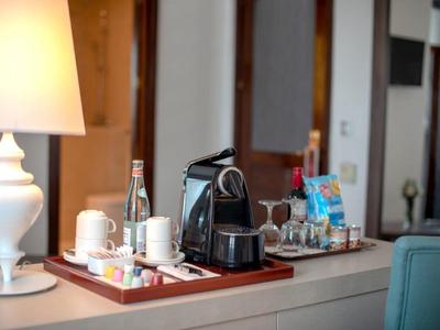 Koffiemachine, kopjes en snacks op een dienblad naast een lamp op een hotelkamertafel.