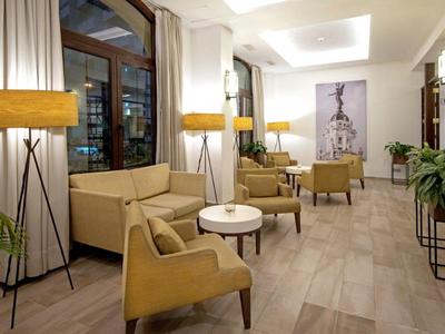 Jasna lobby hotelowa z wygodnymi miejscami do siedzenia, okrągłym stołem i roślinami.