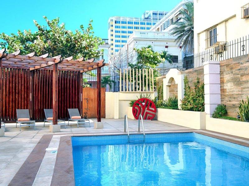 Modern buitenzwembad met ligstoelen en pergola in een hotelomgeving.