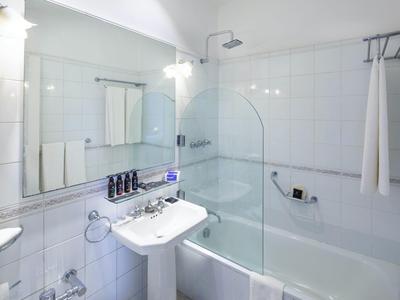 Salle de bain d'hôtel moderne avec lavabo, baignoire, cabine de douche et mur miroir.