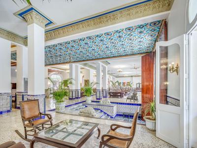 Helle Hotellobby mit bunten Deckenfliesen, Sitzbereich und Pflanzen.