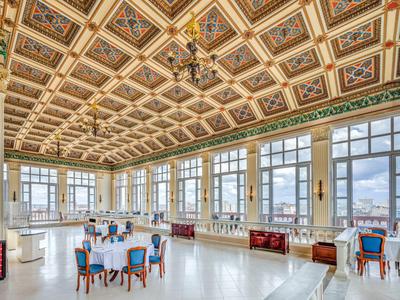 Grande salle de réception avec plafond à caissons orné et tables élégantes près des fenêtres.