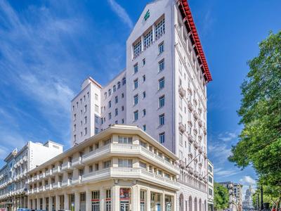 Haut bâtiment d'hôtel avec façade blanche et balcons rouges sous un ciel bleu.