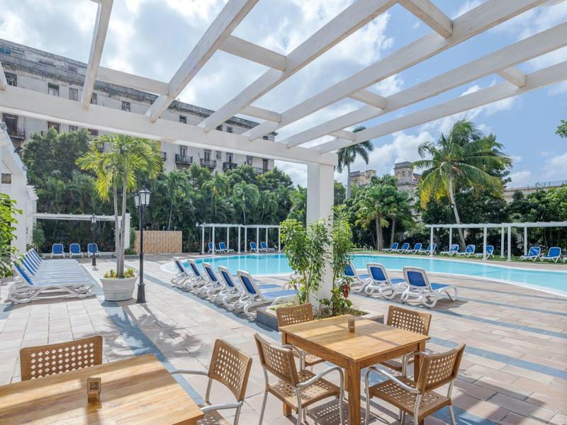 Espace de loisirs avec piscine, transats et coin repas sous pergola.