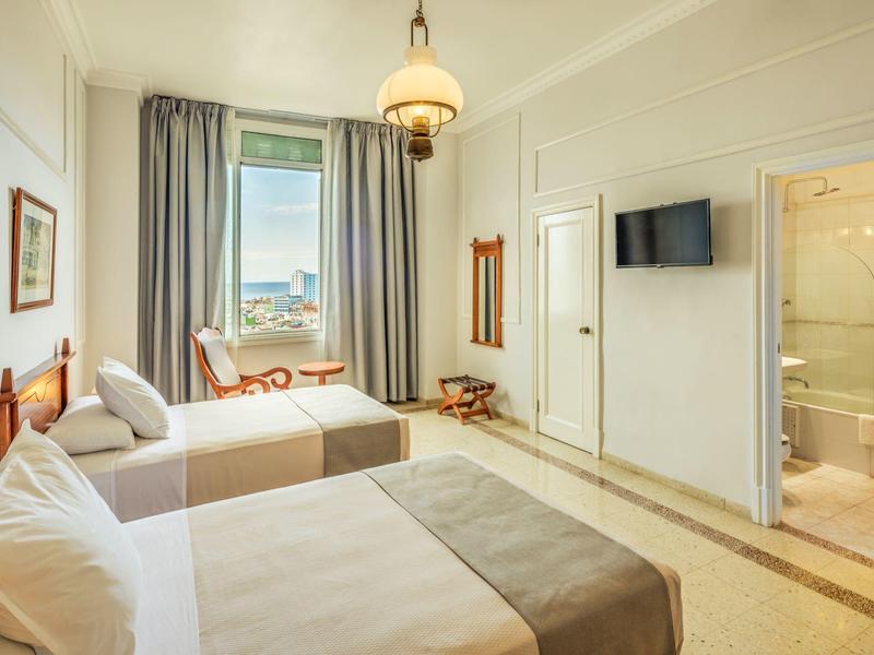 Chambre d'hôtel lumineuse avec deux lits, une vue sur la fenêtre et une salle de bains attenante.