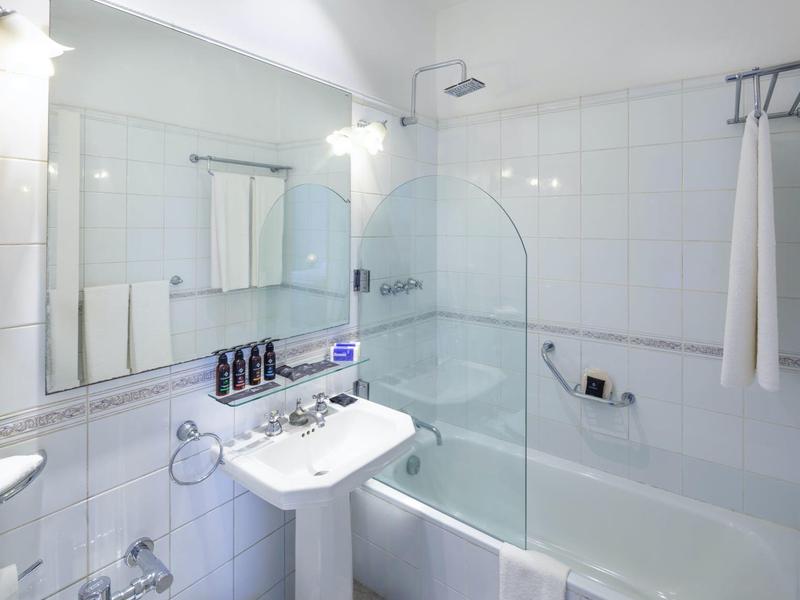 Salle de bain d'hôtel moderne avec lavabo, baignoire, cabine de douche et mur miroir.