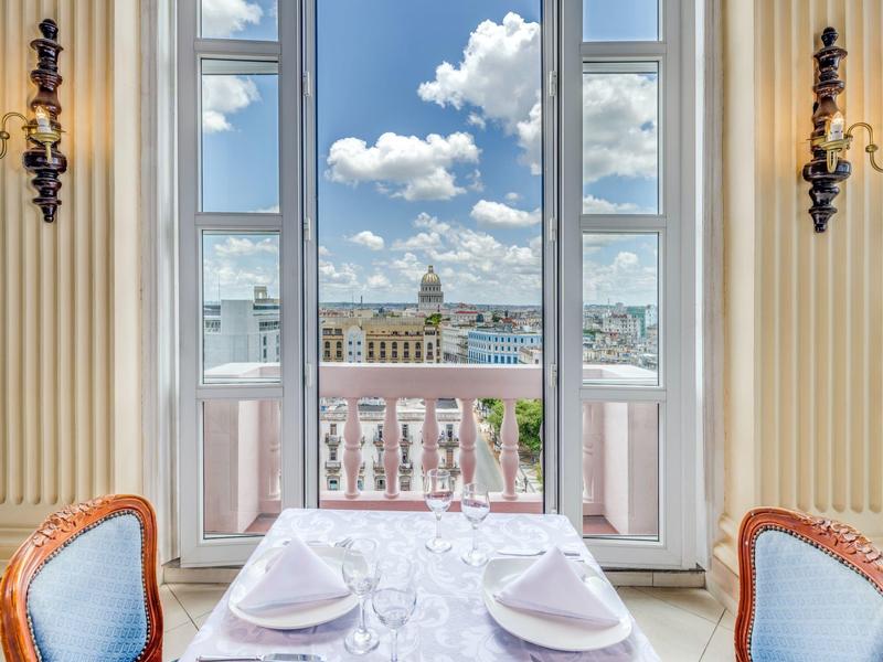 Salle à manger élégante avec vue sur la ville à travers de grandes fenêtres et un balcon.