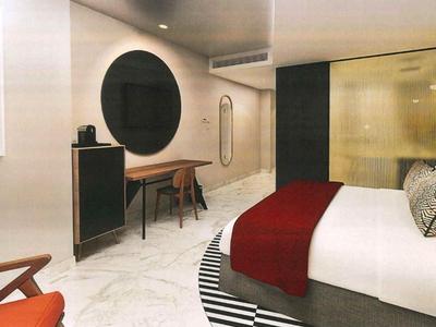 Modern hotel room with double bed, red carpet, and cozy seating area.