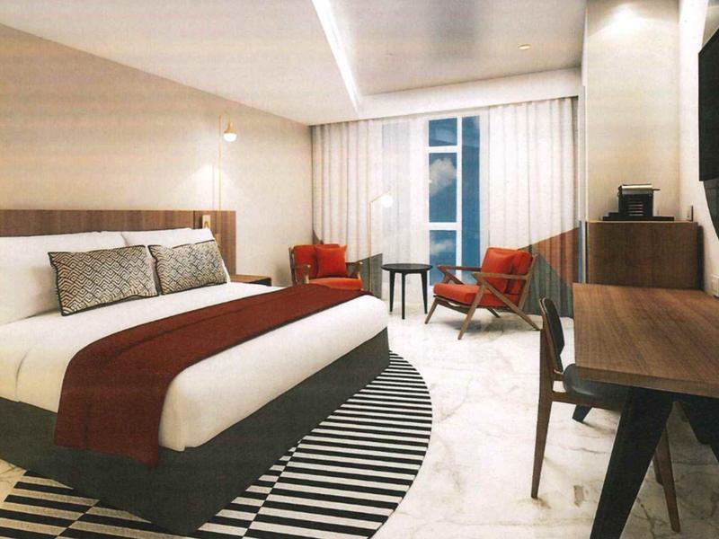 Modern hotel room with large bed, desk, and seating area in natural light.