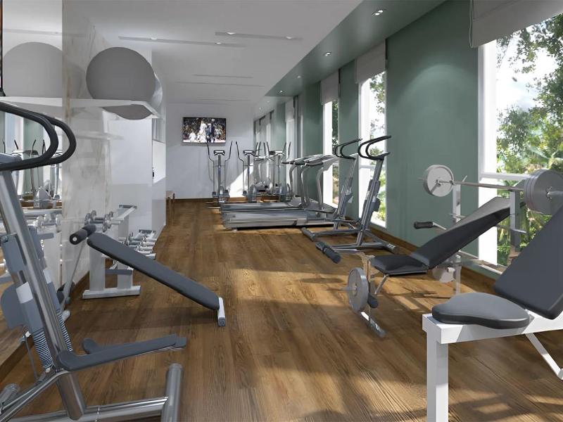 Modern gym with wood flooring, equipment, and large windows overlooking greenery.