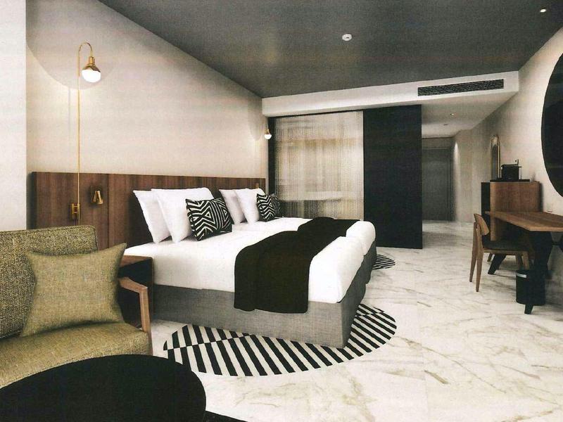 Modern hotel room with double bed, armchairs, and desk in neutral colors.