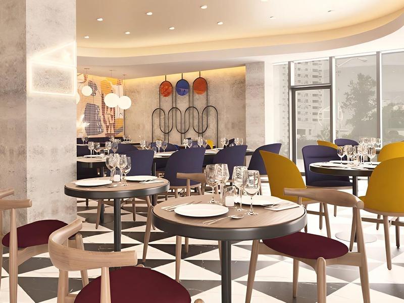 Modern hotel restaurant with colorful chairs and round tables.