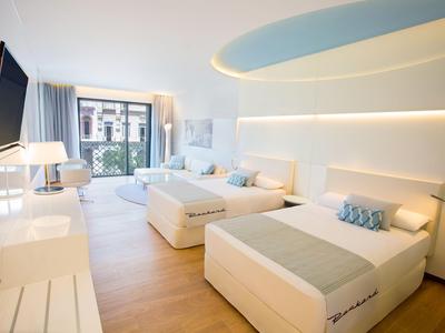 Camera d'hotel moderna con due letti singoli, zona salotto e grande finestra con vista sulla città.