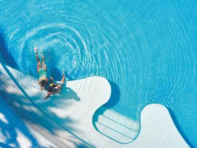 Persona che nuota in una piscina azzurra chiara con scalini e ombre nell'acqua.