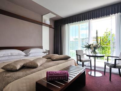 Modernes Hotelzimmer mit Doppelbett, Sesseln, Tisch und großer Fensterfront mit Blick nach draußen.