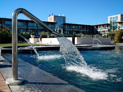 Moderner Pool mit Wasserdusche und Hotelgebäude im Hintergrund bei Sonnenschein