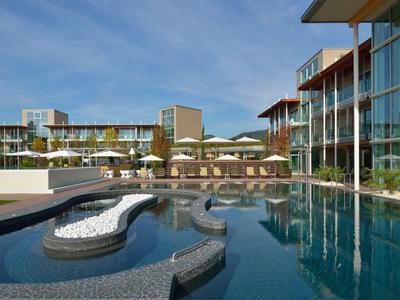 Moderner Hotelpool mit luxuriösen Liegeflächen und gläsernem Gebäude im Hintergrund unter blauem Himmel.