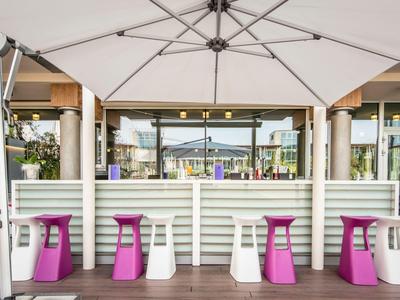 Moderne Outdoor-Bar mit weißen und lila Hockern unter großen Sonnenschirmen
