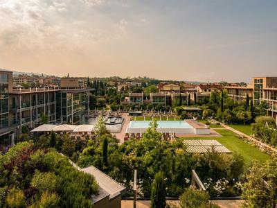 Moderner Hotelkomplex mit zwei Gebäuden, Pool und begrünter Gartenanlage bei Sonnenuntergang.