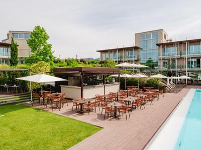 Moderner Hotelpoolbereich mit Holzterrasse, Tischen, Stühlen und Sonnenschirmen bei bewölktem Himmel.