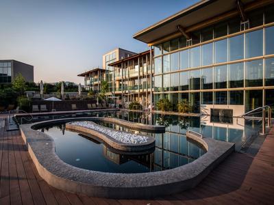 Modernes Hotel mit Glasfassade, umlaufendem Pool und Holzdeck in ruhiger Umgebung bei Sonnenuntergang.