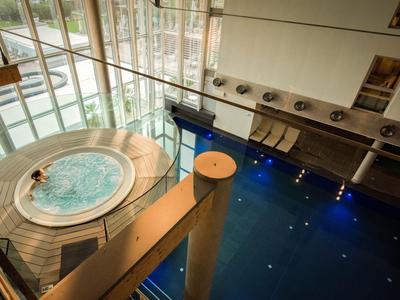 Moderner Whirlpool neben einem blauen Innenpool mit großen Fenstern und Holzboden