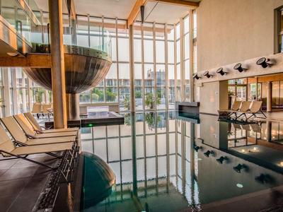 Innenpoolbereich eines Hotels mit Holzliegen und großer Panoramaverglasung.