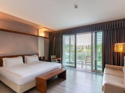 Modernes Hotelzimmer mit großem Bett, Sitzbank, Sofa und Balkon mit Blick auf die Natur.