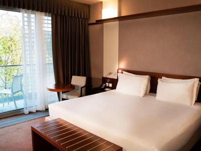 Modernes Hotelzimmer mit Doppelbett, Balkon und Blick auf Bäume.