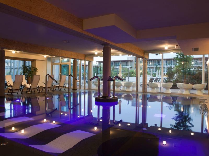 Moderner Indoor-Pool mit Lounge-Bereich und blauer Beleuchtung in einem Hotel.
