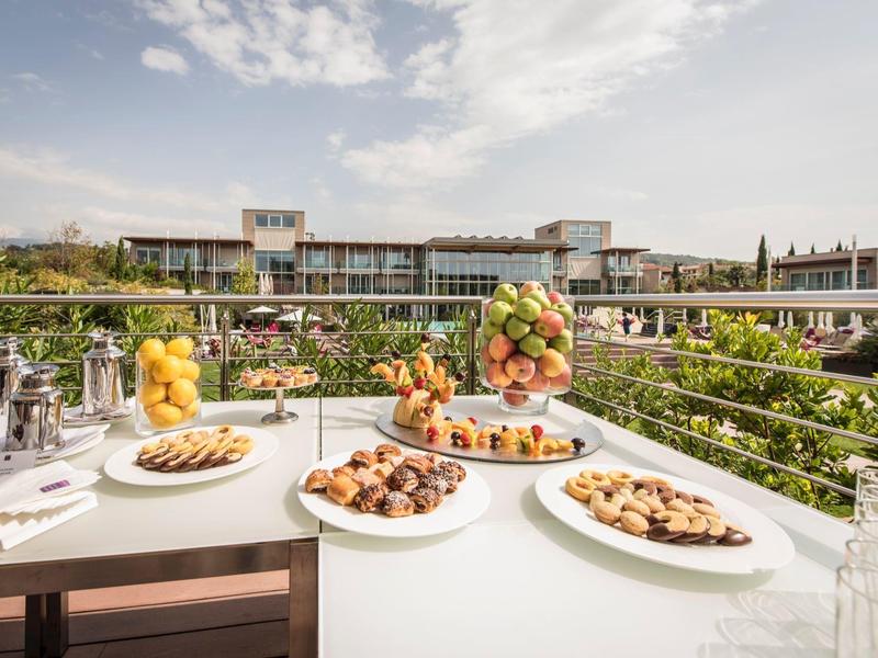 Tisch mit Gebäck und Obst auf der Hotelterrasse mit Aussicht auf das Hotel und den Himmel.