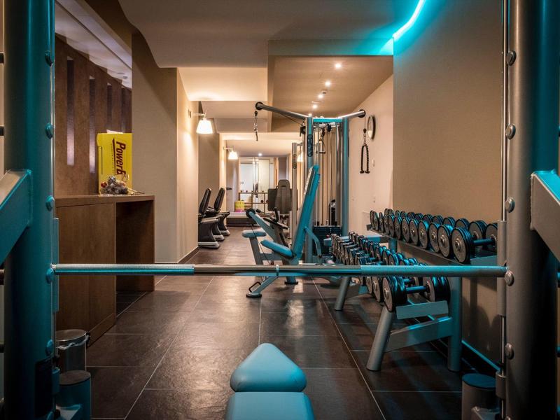 Moderner Fitnessraum mit Kraftgeräten, Hanteln und Beleuchtung in einem Hotel.
