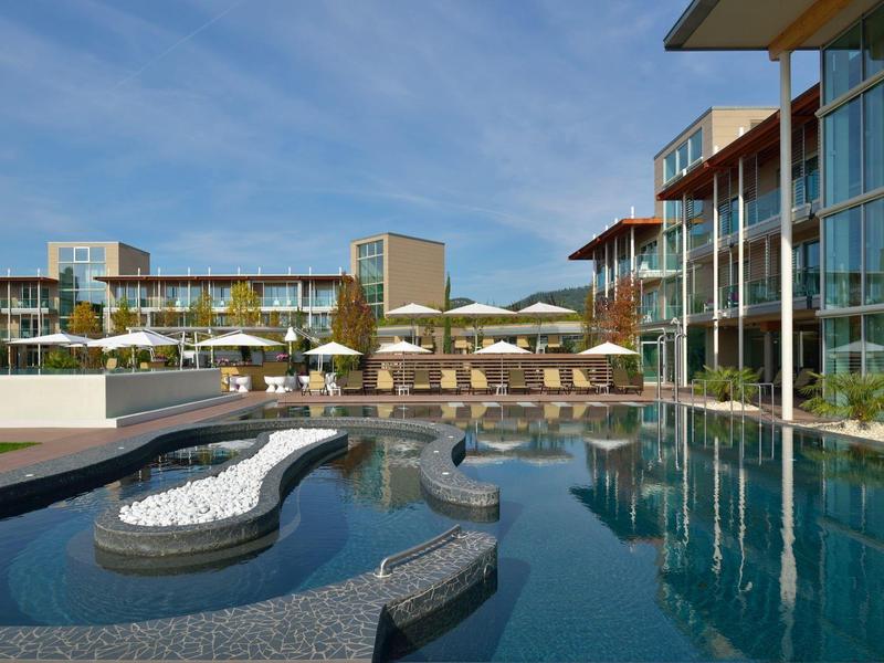 Moderner Hotelpool mit Liegen und Glasfassaden unter blauem Himmel.