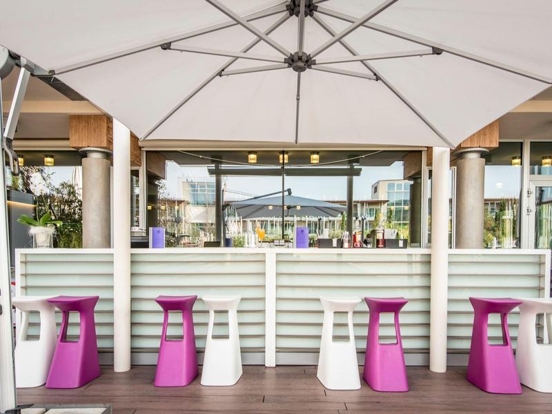 Moderne Outdoor-Bar mit weißen und lila Hockern unter großen Sonnenschirmen