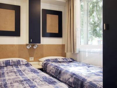 Twin room with blue bedcovers, wooden panels, and a window with curtains