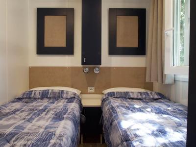 Hotel room with two single beds, each with checkered bedspreads, and two unframed pictures on the wall.