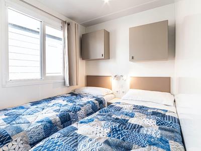 Bright bedroom with two single beds, blue patterned bedspreads, and a window with curtain.