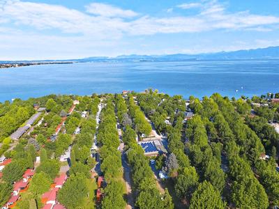 Aerial view of trees and buildings along the coast with sea and mountains in the background.