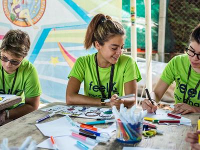 Three young people sit at a table and color together using various markers.
