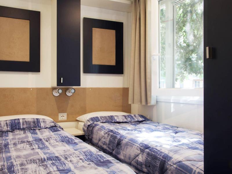 Twin room with blue bedcovers, wooden panels, and a window with curtains
