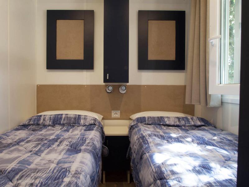 Hotel room with two single beds, each with checkered bedspreads, and two unframed pictures on the wall.