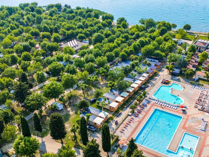Aerial view of a resort with pools, sun terraces, and lush greenery near the water.