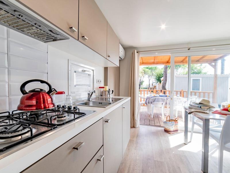 Bright kitchen with gas stove, red kettle, and view of terrace with garden furniture.
