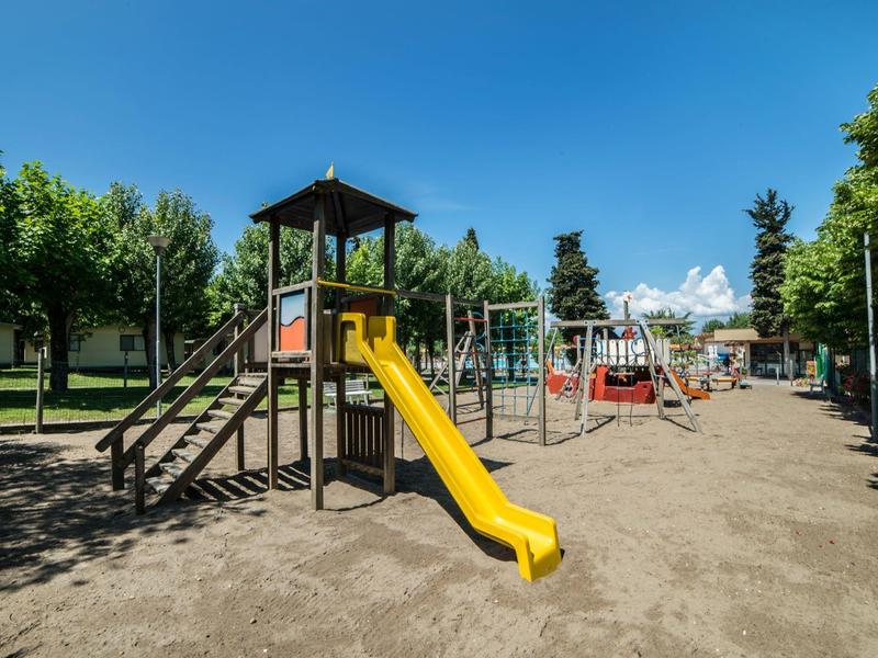 A playground with climbing structure, slide, and swings under blue sky and trees.