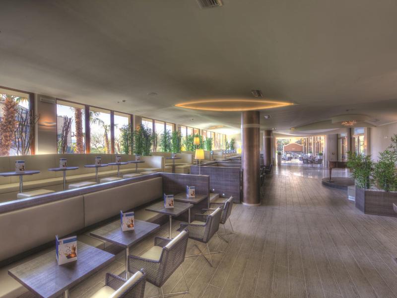 Area lounge di hotel moderna con divani in pelle, sedie e tavoli decorati con piante.